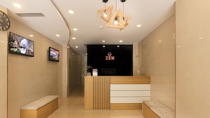 A reception area with a wooden reception desk, two wall-mounted televisions, and a bench. - Zen Hotel (Nha Trang)