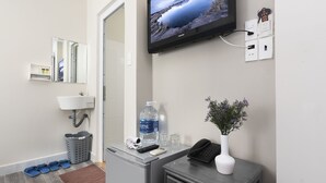 A hotel reception area with a flat-screen TV, a telephone, a water dispenser, a waste basket, and a vase with flowers. - Zen Hotel (Nha Trang)