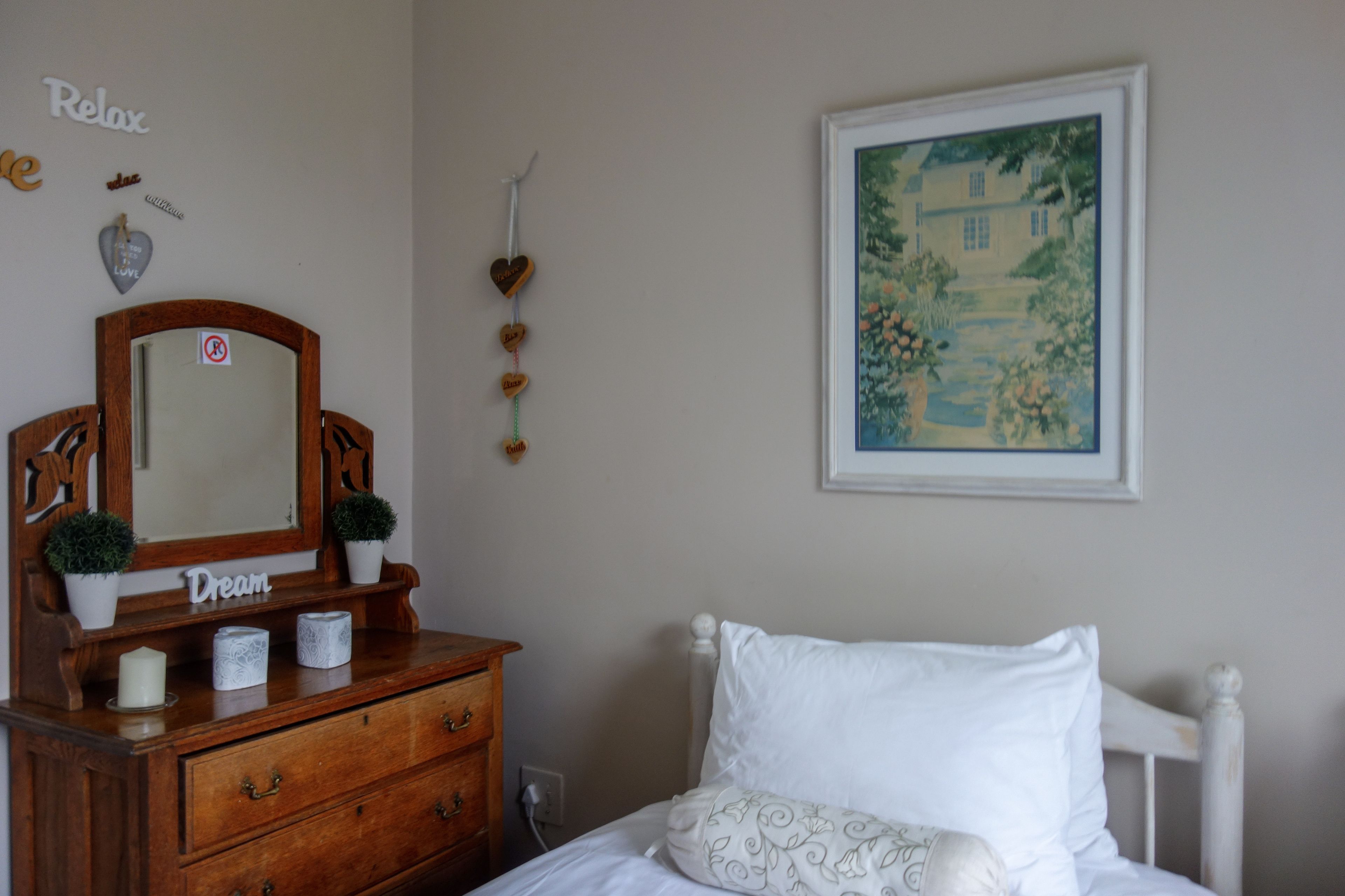 A bedroom with a wooden dresser, a mirror, a framed painting, and a bed with white bedding.