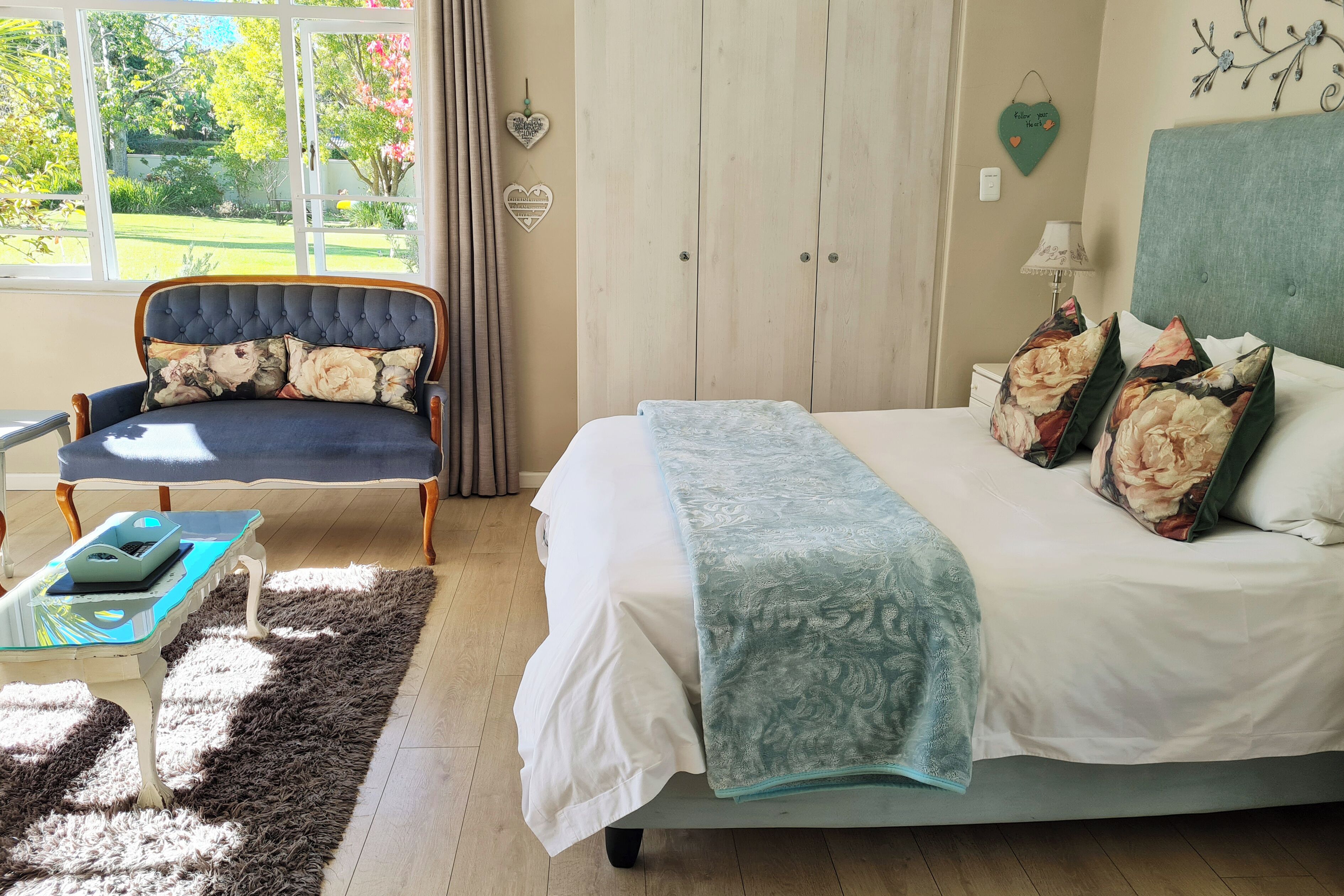 A bedroom with a bed, a chair, a table, and a view of the garden.