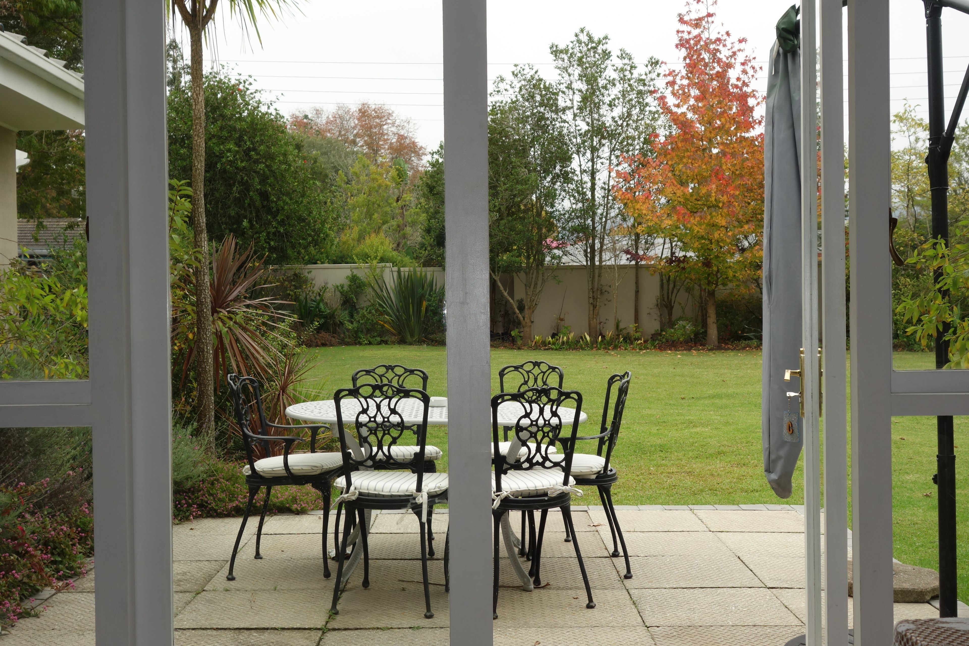 Un patio al aire libre con una mesa y sillas, rodeado de follaje y césped.