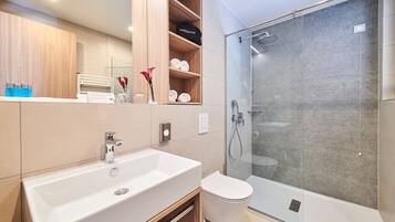 A modern bathroom with a large white sink, a toilet, and a glass-enclosed shower.