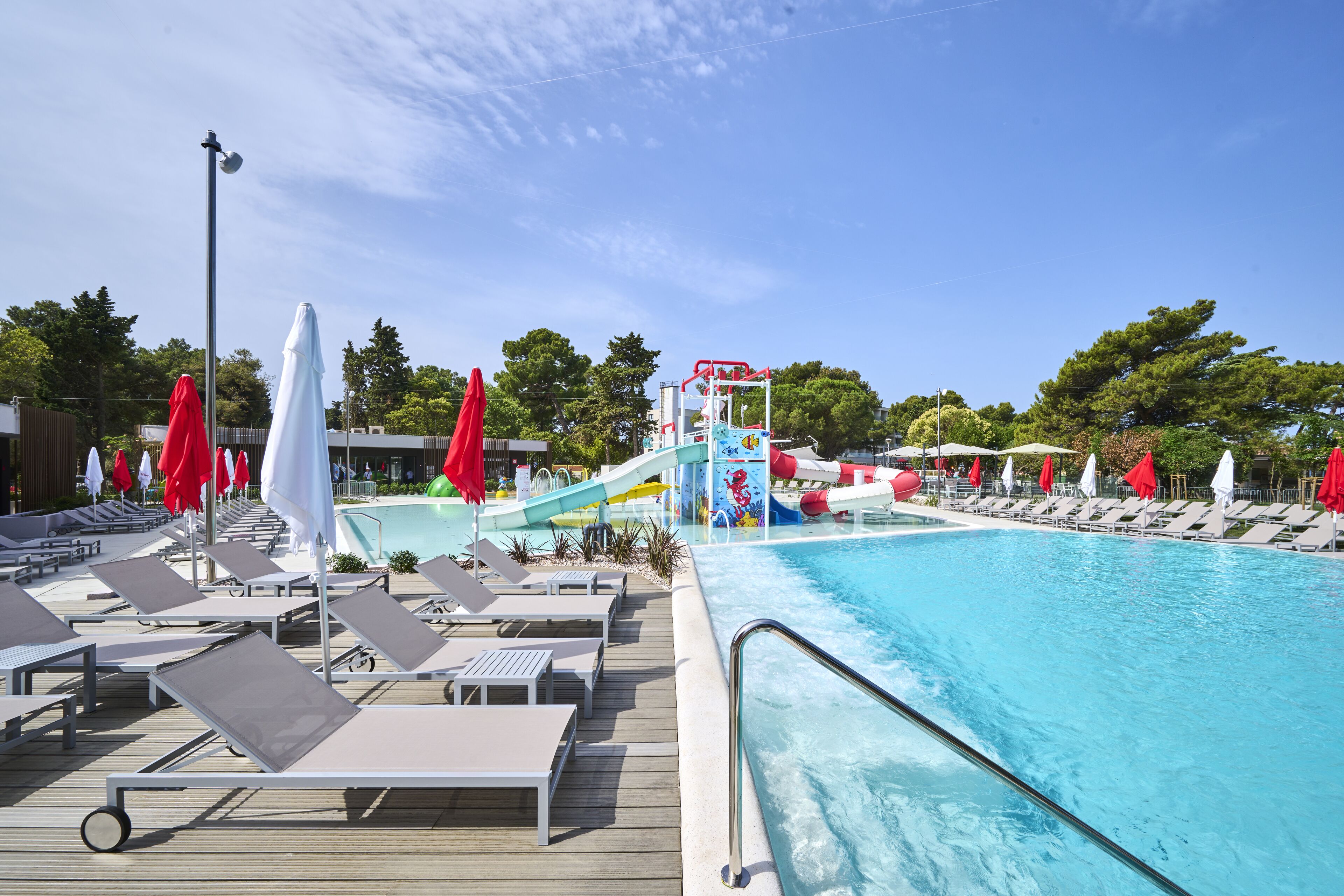 A pool area with lounge chairs, umbrellas, and a water slide.