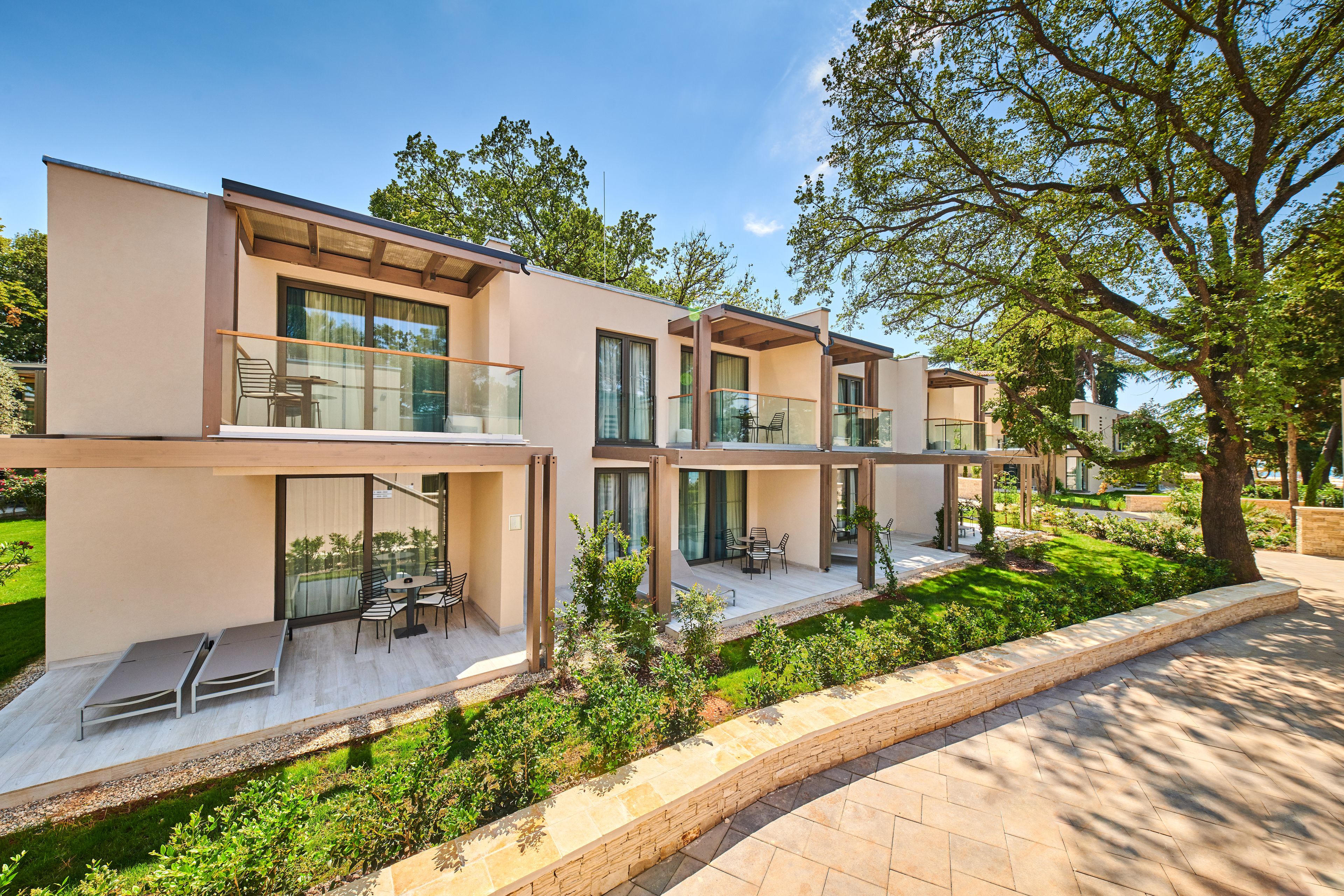 A modern multi-story residential building with balconies, outdoor seating, and a landscaped garden.