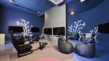 Una habitación moderna con una bicicleta estática Playseat, un sillón de masaje y una zona de comedor con mesa y sillas.