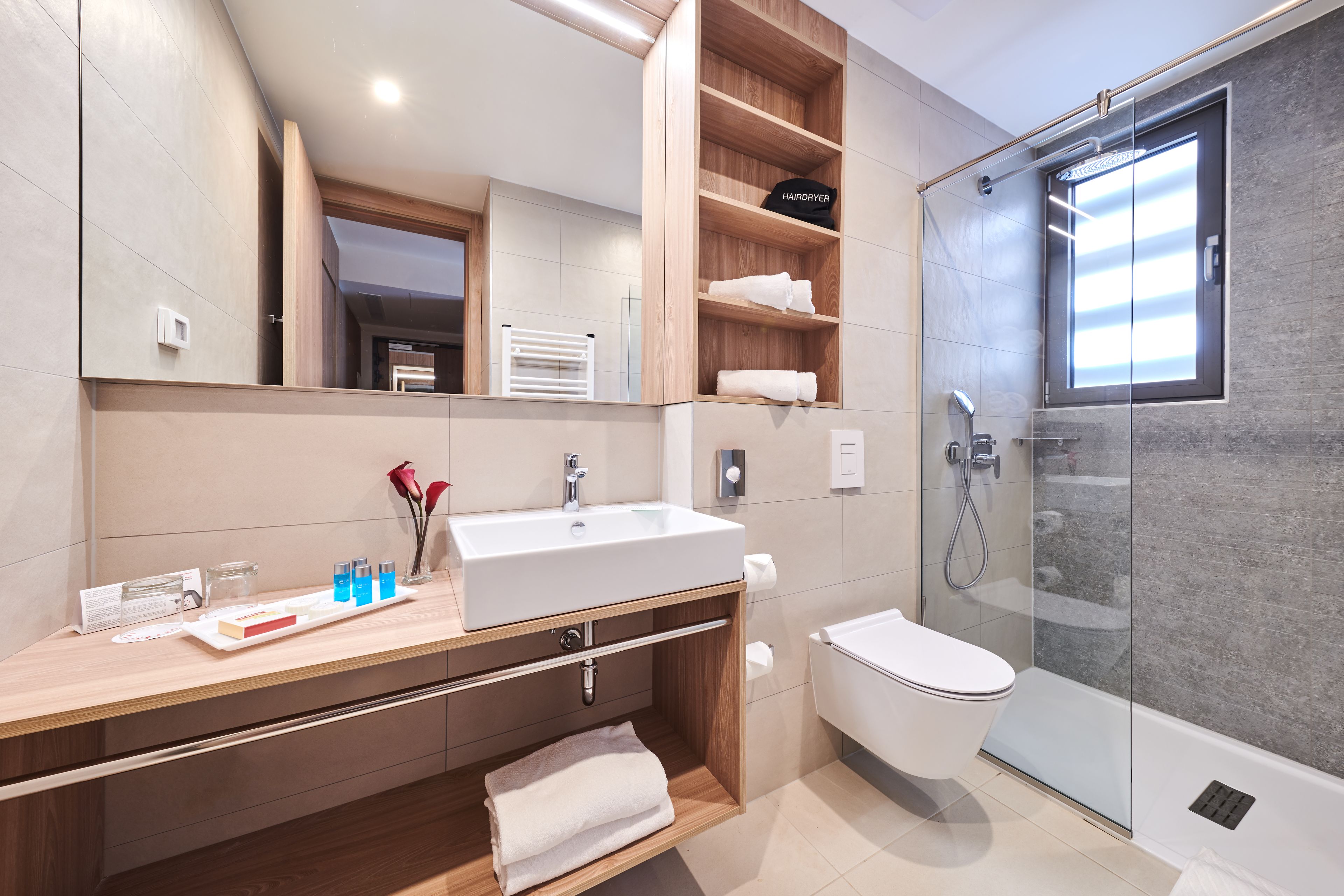 Un baño moderno con un espejo grande, un lavabo blanco, un inodoro y una ducha con mampara de vidrio.