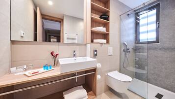 Un baño moderno con un espejo grande, un lavabo blanco, un inodoro y una ducha con mampara de vidrio.