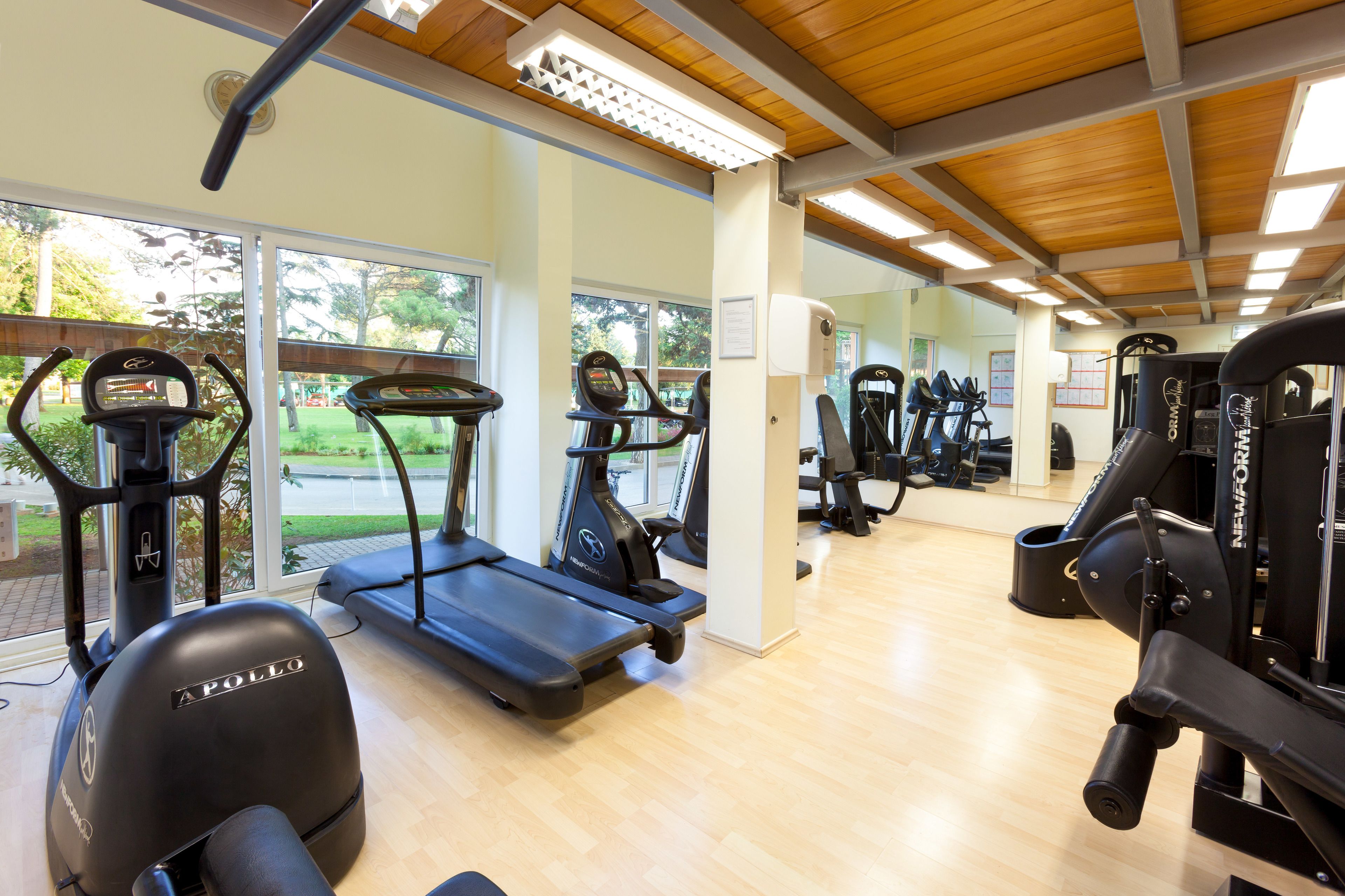 Gimnasio con cintas de correr, máquinas de pesas y un muro de espejos.