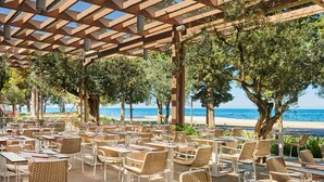 Un área de comedor al aire libre con mesas y sillas, con vista a una playa.