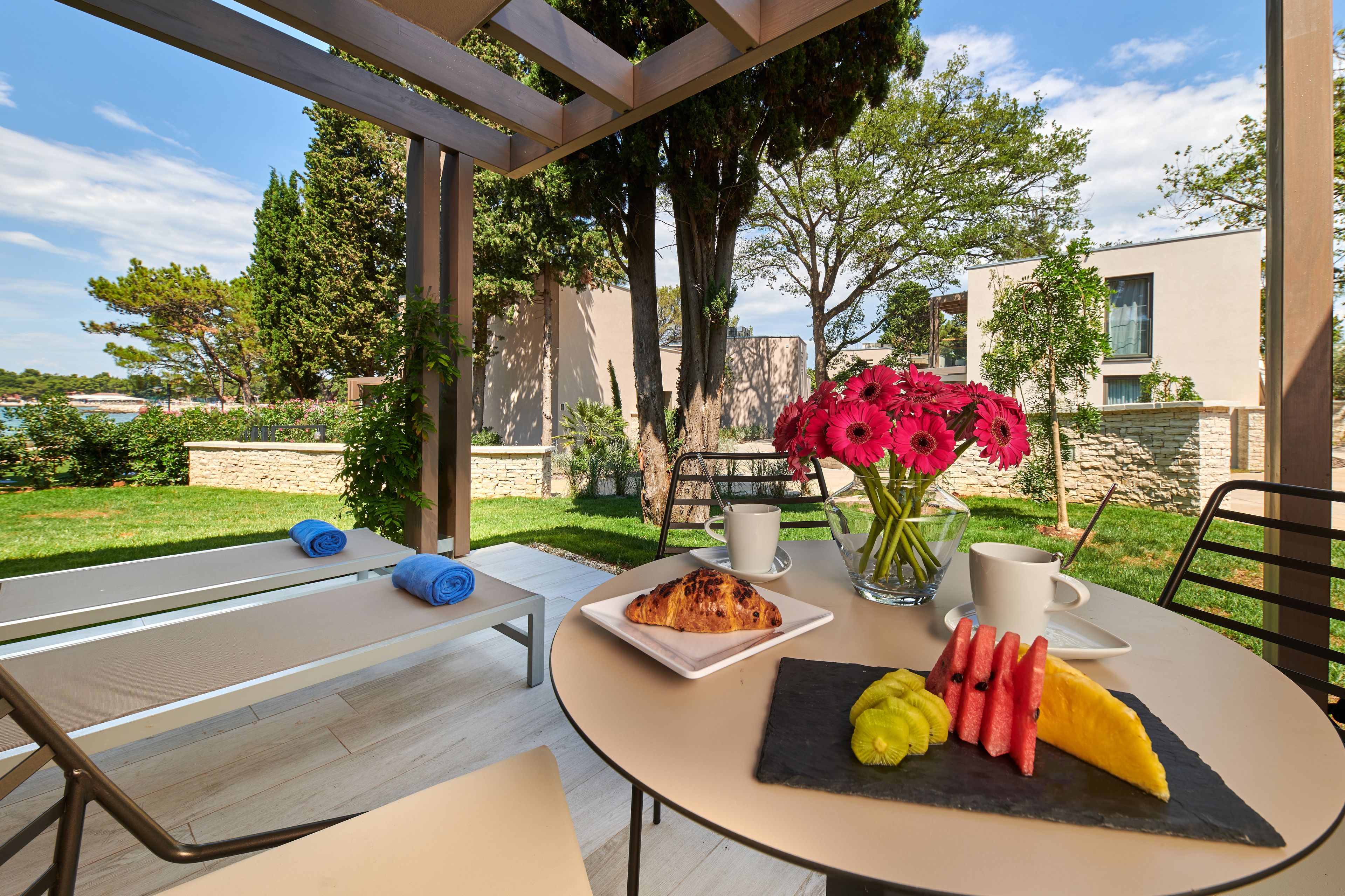 A table set outdoors with a croissant, fruit, and flowers.