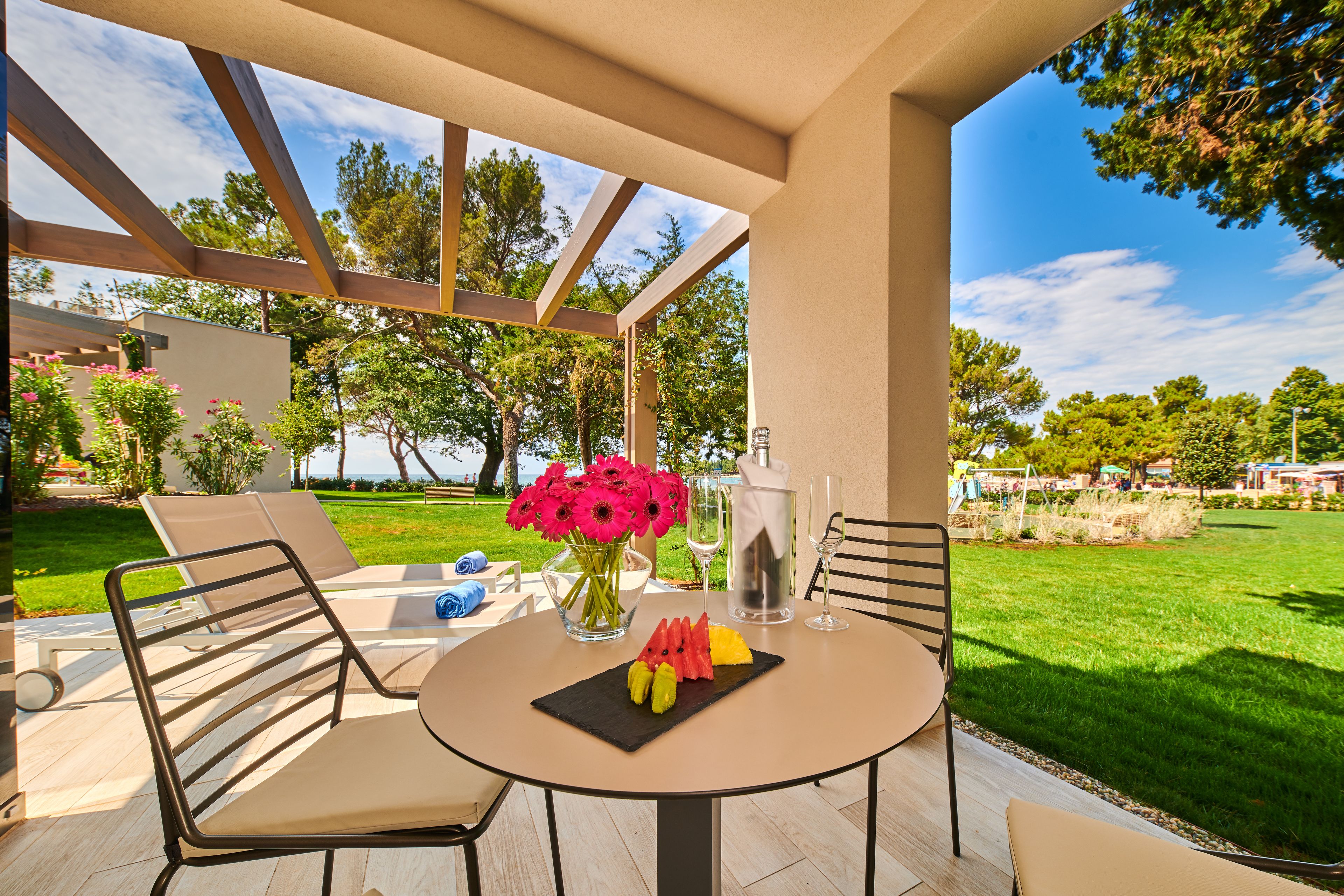 An outdoor patio with a round table, chairs, a vase of flowers, and a glass of water.