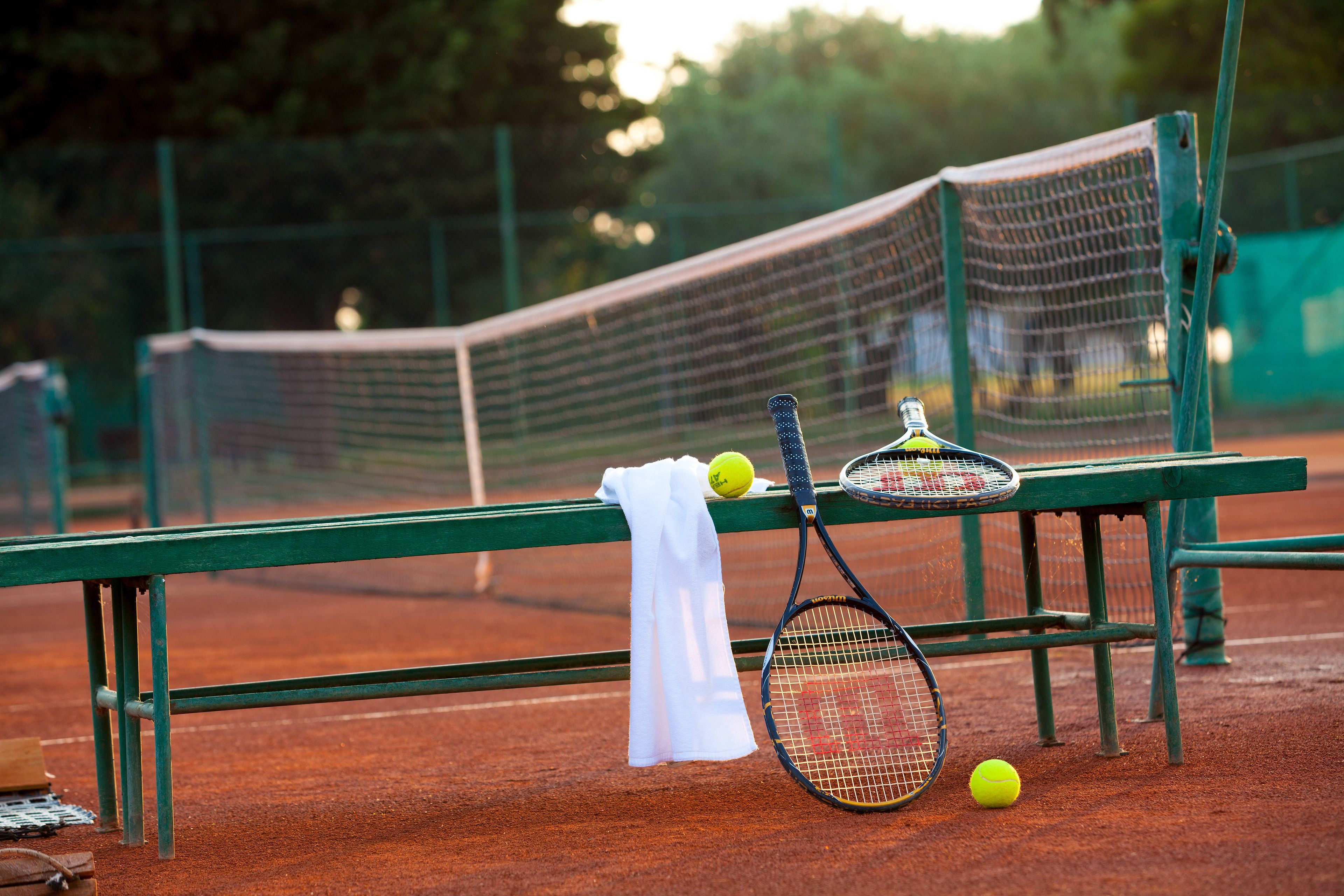 Een tennisbaan met een bankje, twee tennisrackets en drie tennisballen.