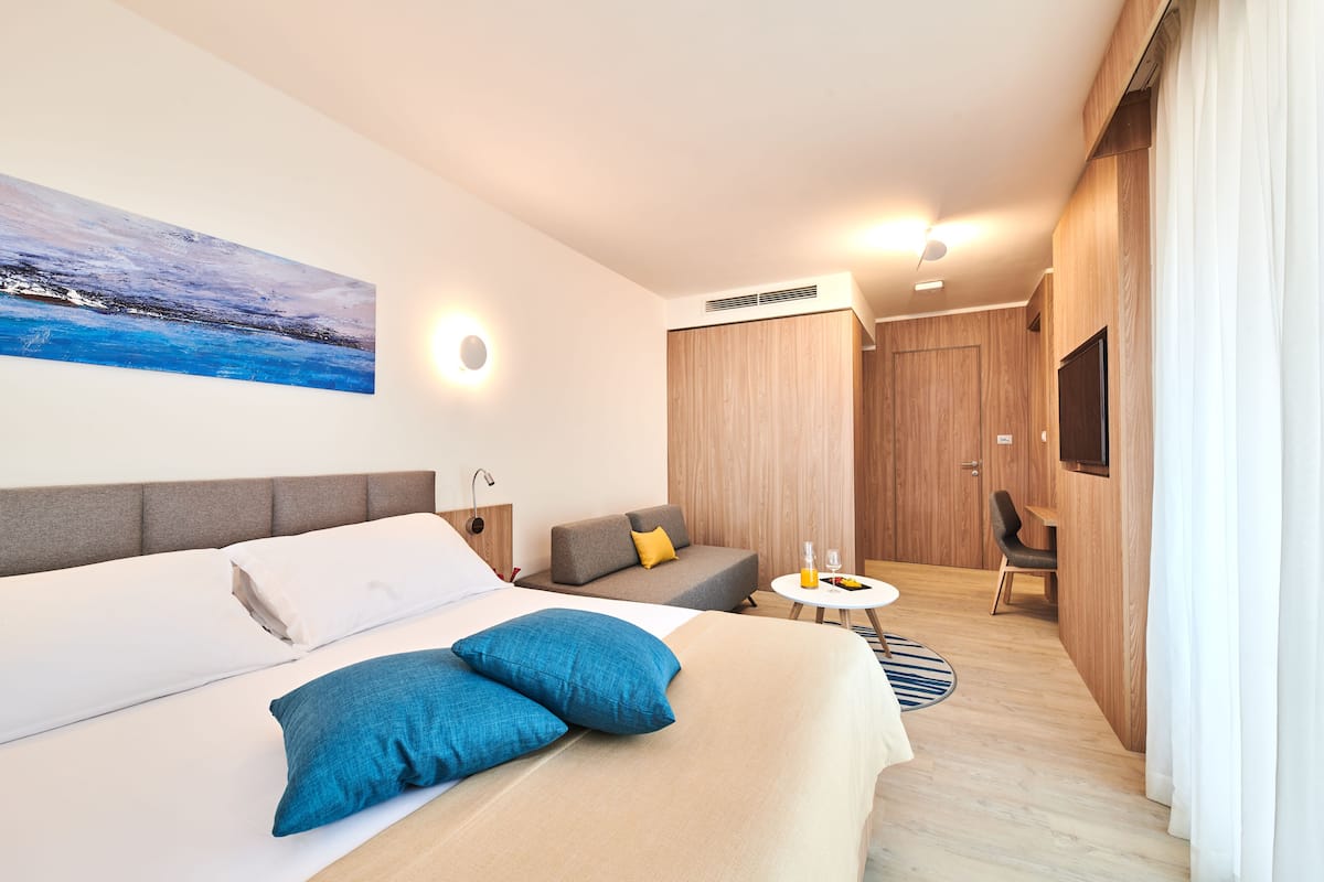 Une chambre d’hôtel moderne avec un grand lit, un canapé, une petite table avec des verres et un téléviseur fixé au mur.