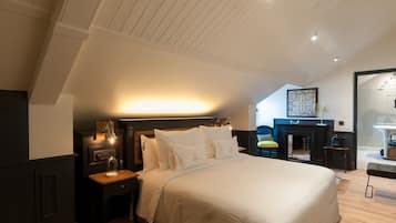 A bedroom with a large bed, a nightstand, a desk, and a fireplace.