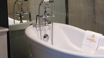 A white freestanding bathtub with a towel labeled "La Casa del Presidente" in a bathroom with a tiled wall and a shower area.