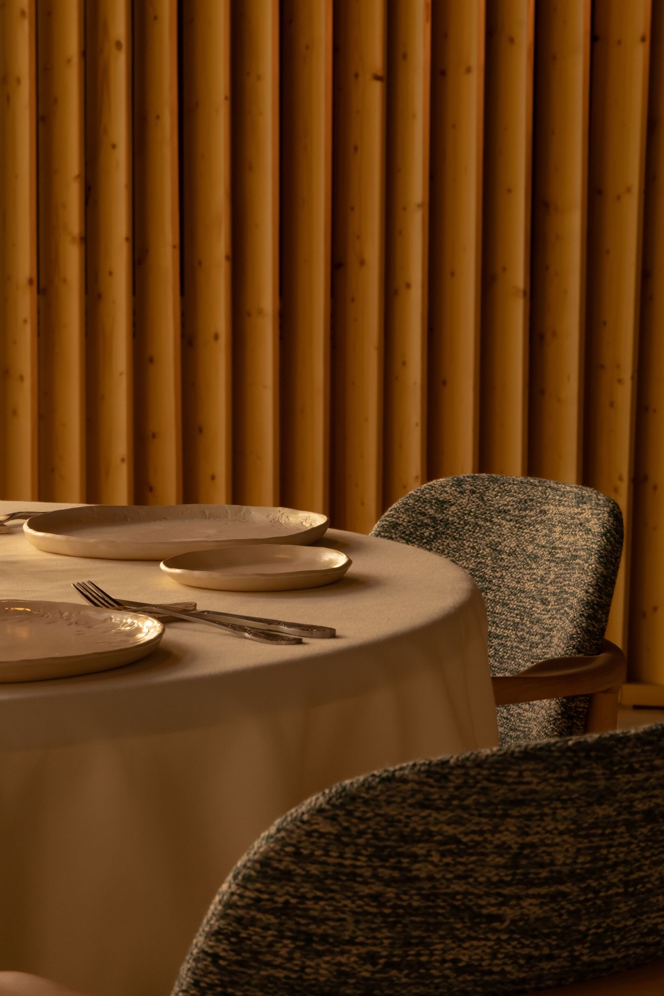 A dining table with plates and cutlery, a chair, and a wooden wall with vertical slats.