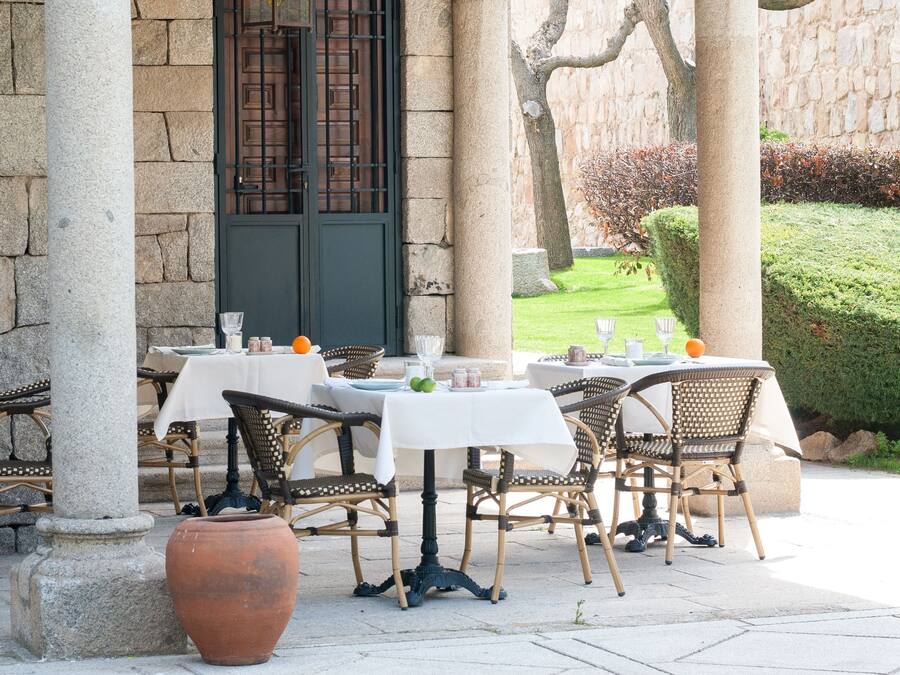 An outdoor patio with tables and chairs, stone columns, and a door with a wrought iron gate.