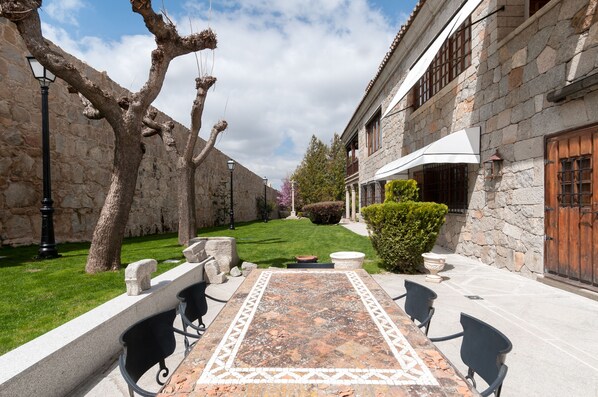 A courtyard with stone walls, a tiled patio, outdoor seating, and a building with a stone facade. - La Casa del Presidente Small Luxury Hotels (Ávila)