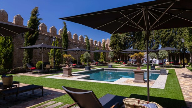 Área de piscina com espreguiçadeiras, guarda-sóis e um muro de pedra ao fundo.