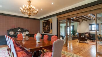 A spacious dining room with a large wooden table, red upholstered chairs, a chandelier, and a painting on the wall.