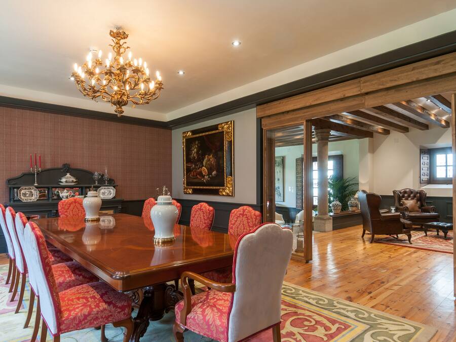 A spacious dining room with a large wooden table, red upholstered chairs, a chandelier, and a painting on the wall.