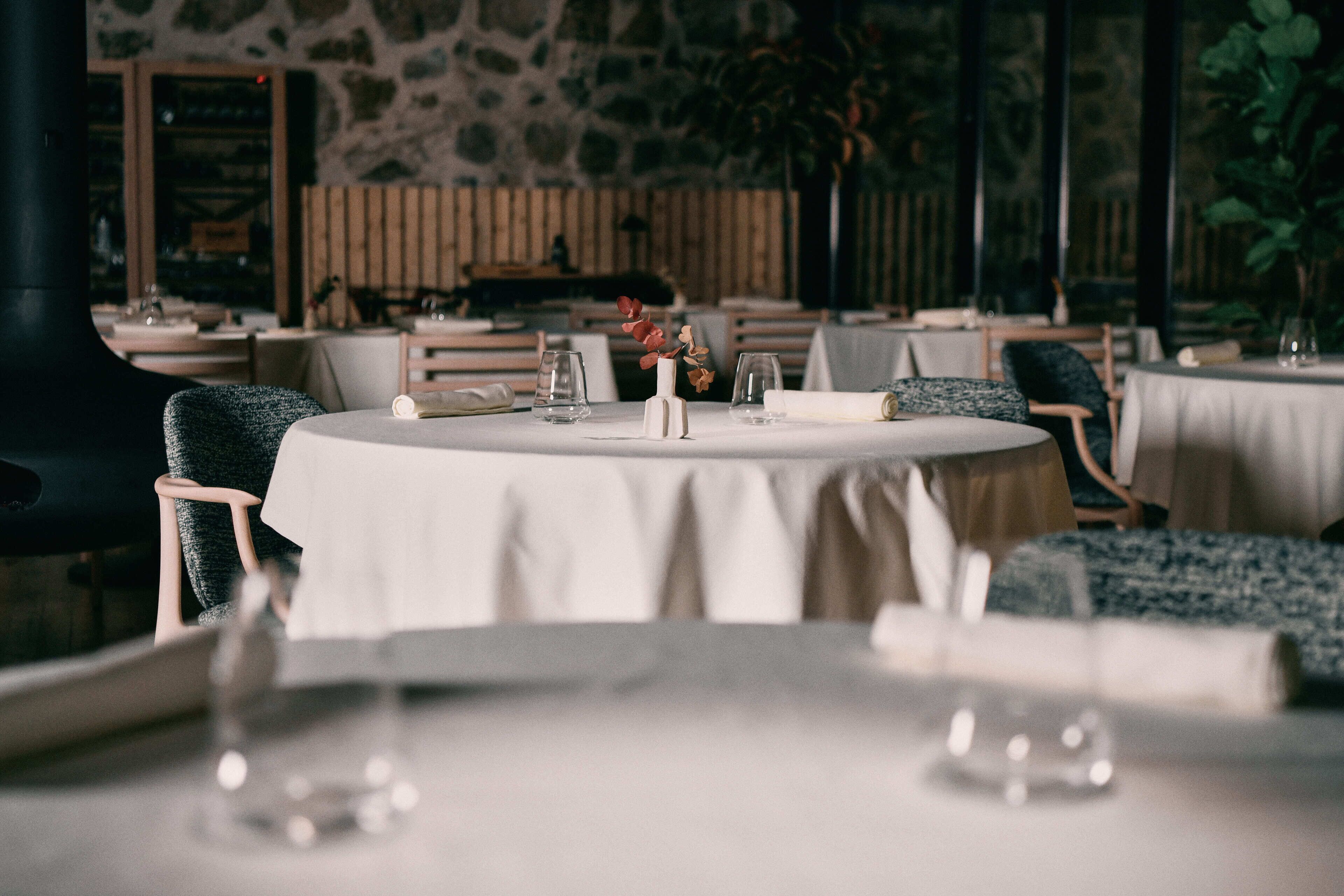 A restaurant with round tables, chairs, and a stone wall in the background.
