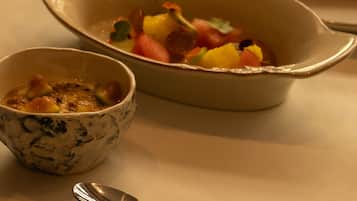 Una mesa de comedor con diversos platos, incluyendo un tazón de ensalada de frutas, un bol de sopa y un plato con un omelette enrollado.