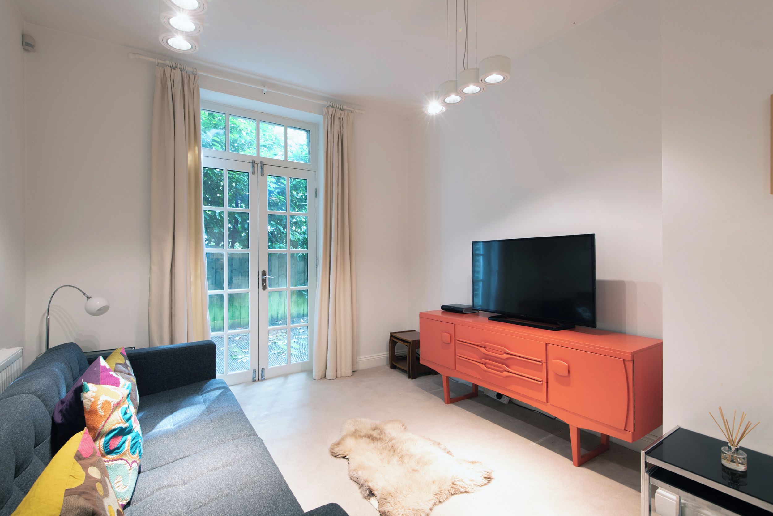 A modern living room with a sofa, a television, a red cabinet, and a large window with curtains.