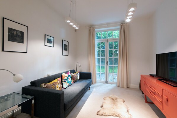 A modern living room with a sofa, a glass coffee table, a red TV stand, and a large window with curtains.