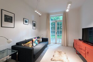 Una sala moderna con un sofá, una mesa de centro de vidrio, un mueble de TV rojo y un ventanal con cortinas.