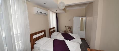 A hotel room with two beds, a wooden headboard, a white air conditioning unit, a white wardrobe, and a wooden nightstand.