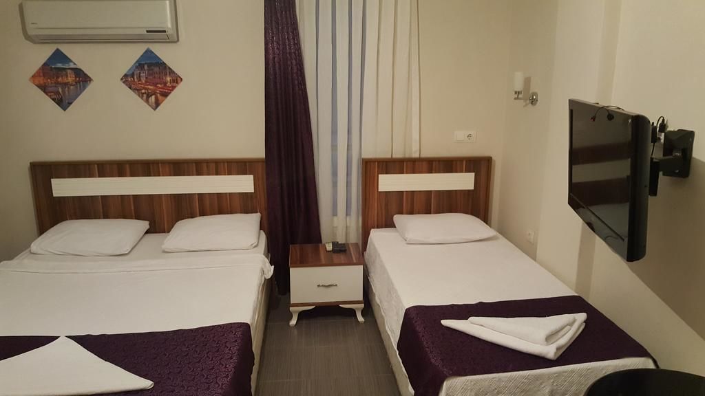 A hotel room with two beds, a TV, a small table, and a window with curtains.
