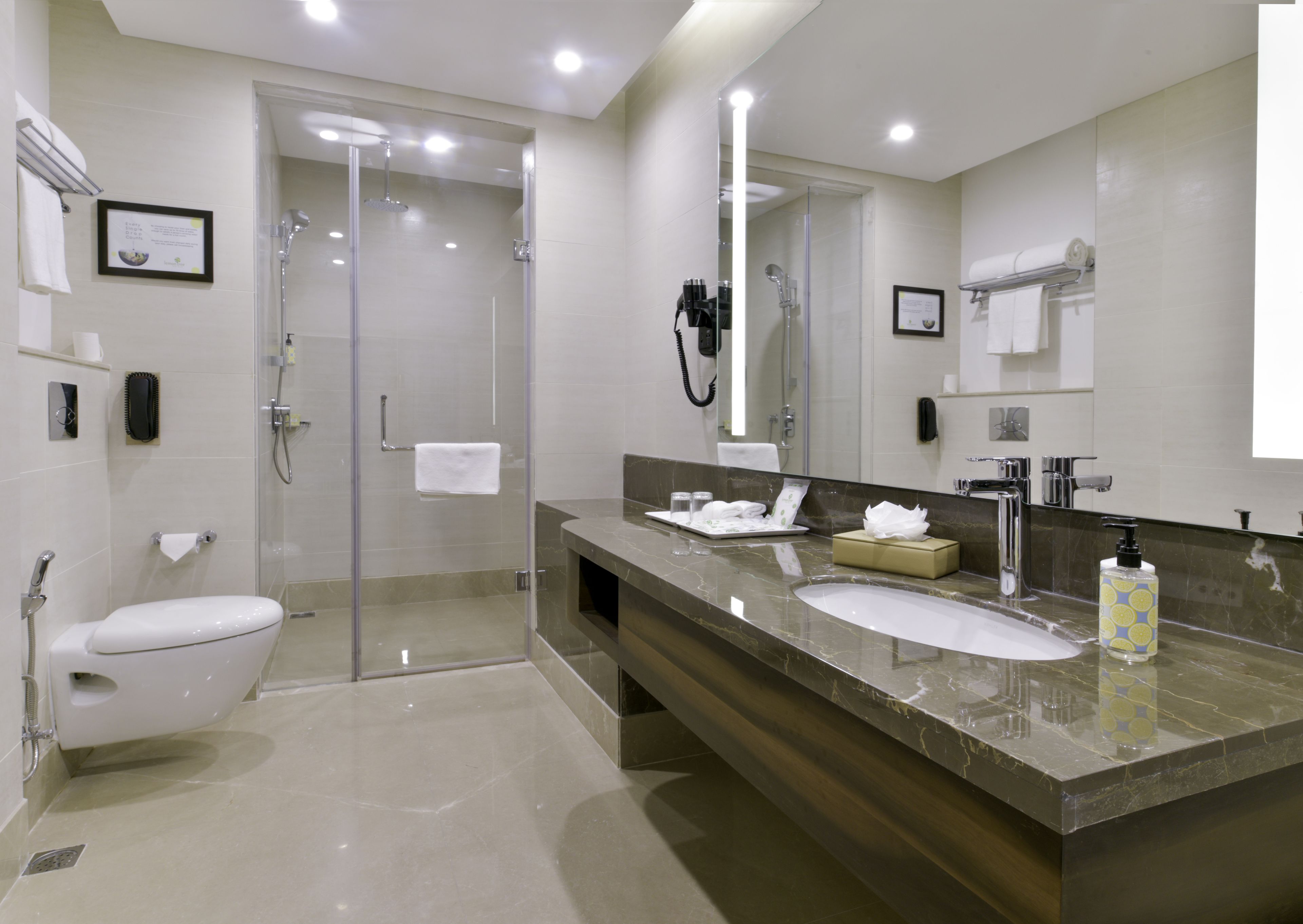 A modern bathroom with a glass-enclosed shower, a white toilet, a marble vanity with two sinks, and a large mirror.