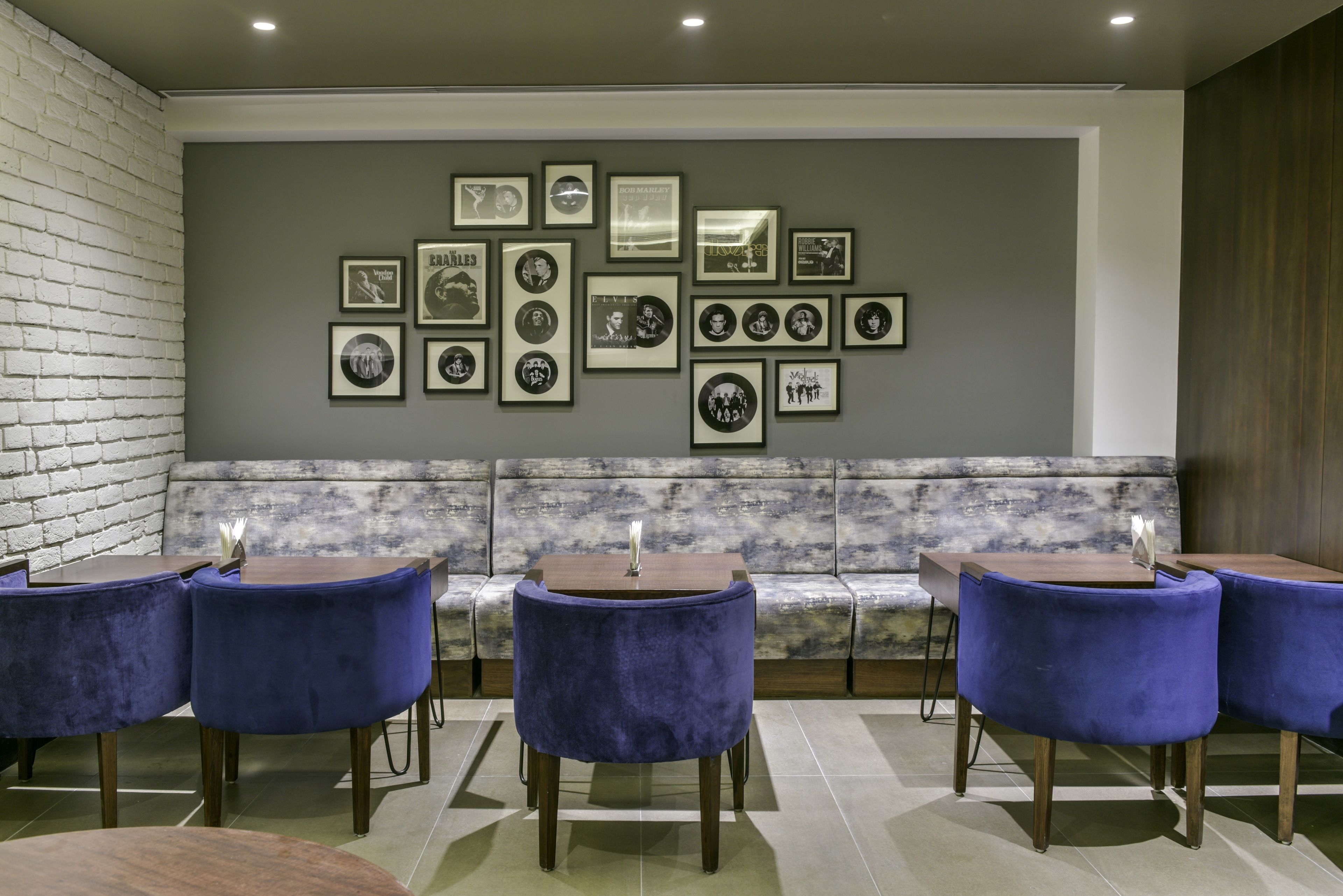 A modern lounge area with a marble bench, blue velvet chairs, and a wall decorated with framed black and white photographs.