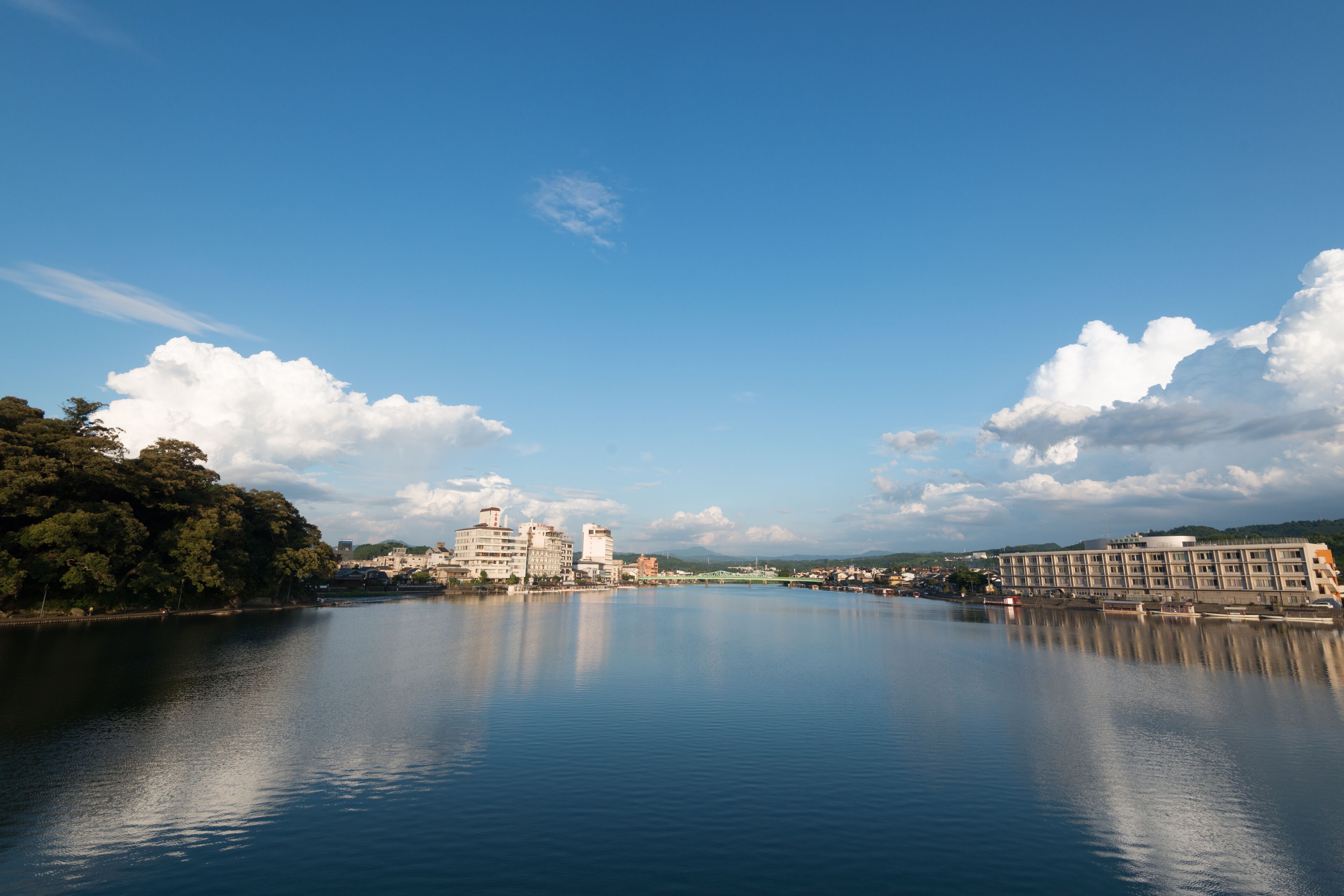 A calm river with buildings on the banks, including a large hotel with multiple floors and a smaller building nearby.