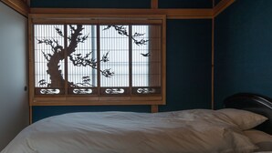 Una habitación con una cama, un ventanal con un diseño de árbol y una pared azul oscuro.