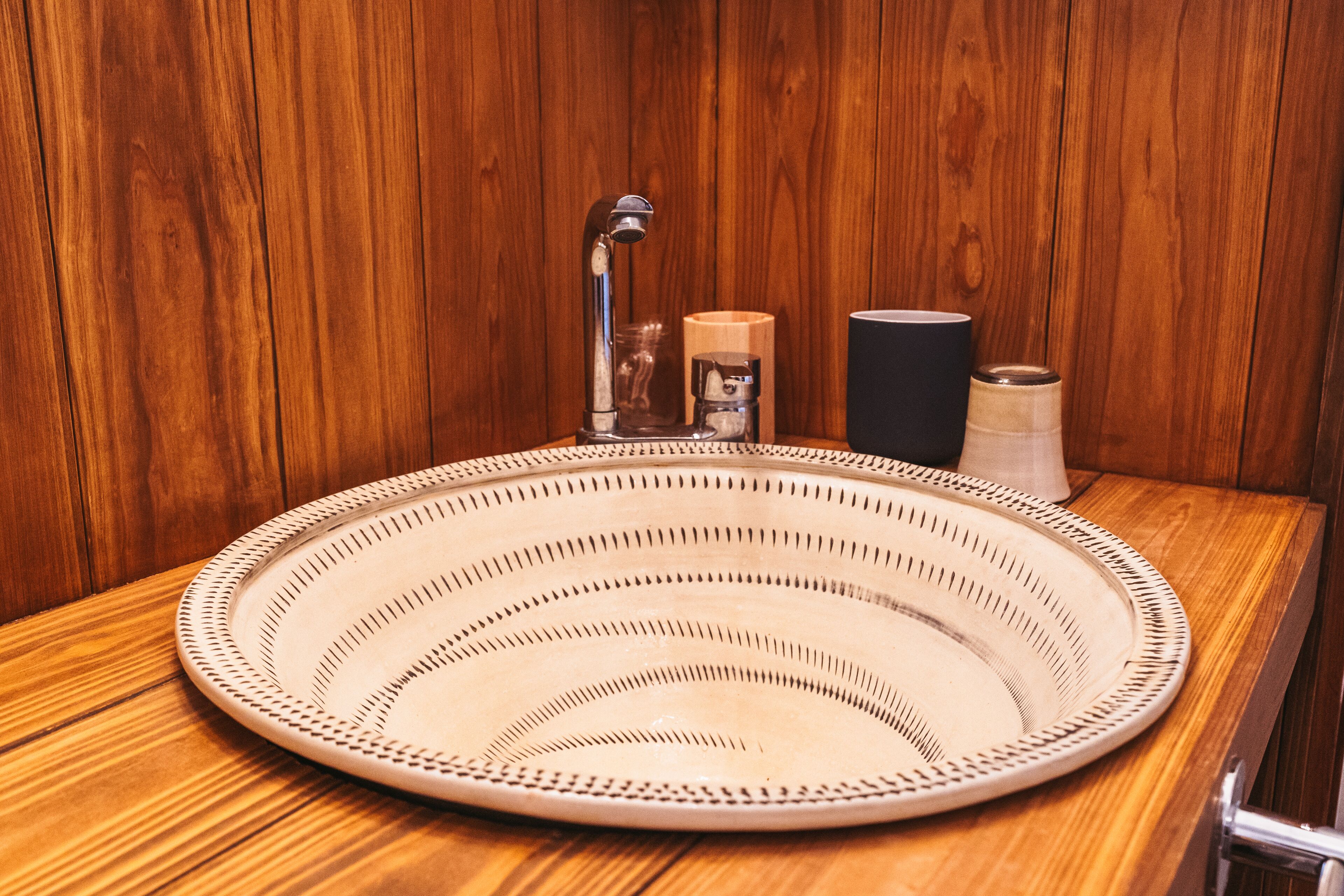 A round, woven sink with a faucet and soap dispenser, set against a wooden wall.