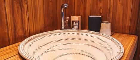 A round, woven sink with a faucet and soap dispenser, set against a wooden wall.