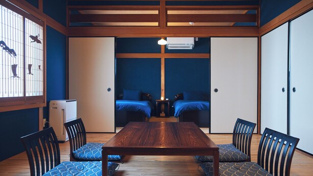 Una habitación tradicional japonesa con una mesa de madera, cojines de estampado azul y puertas correderas.