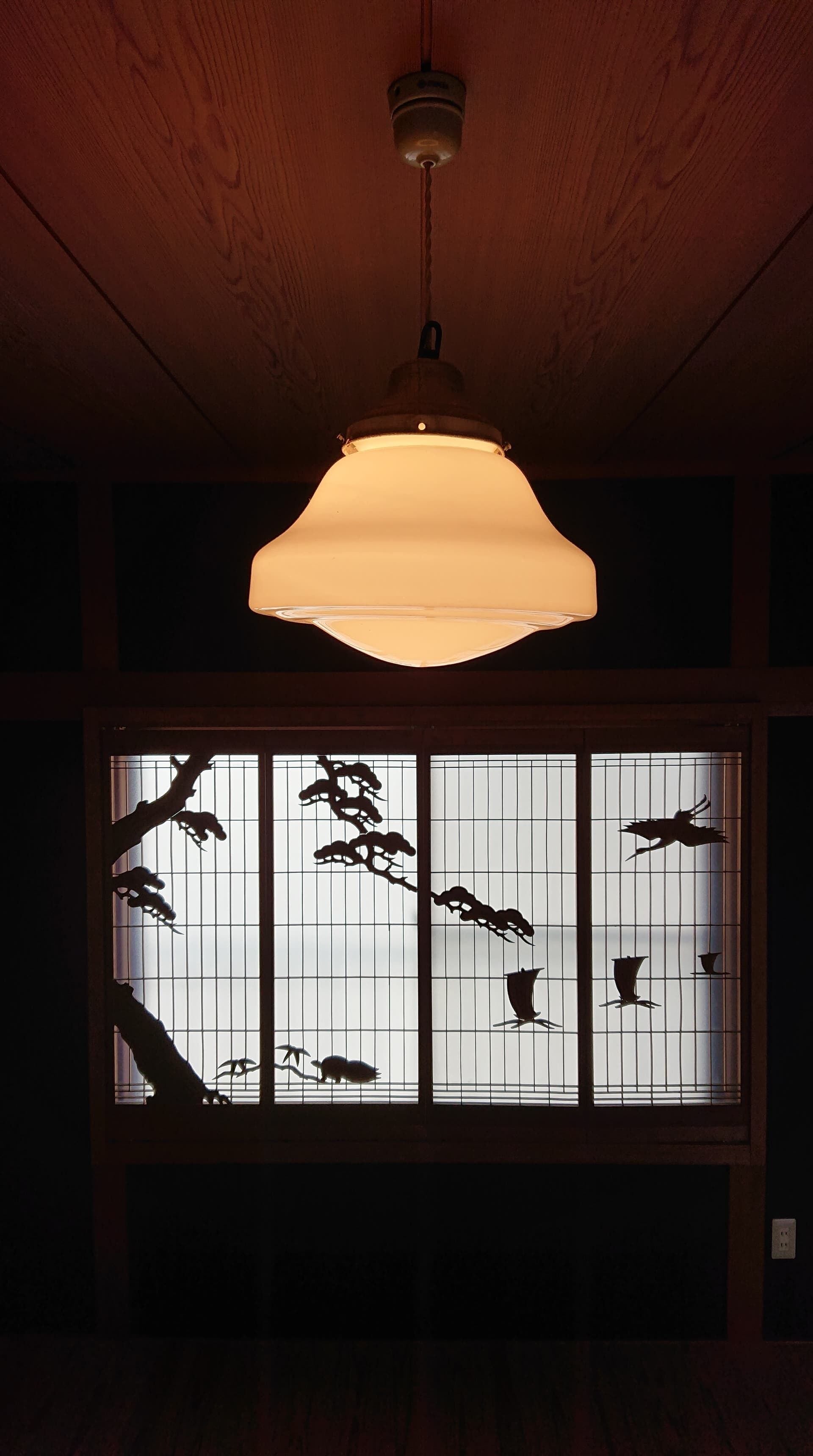 A traditional Japanese room with a wooden ceiling, a hanging light fixture, and a shoji screen with silhouettes of birds and branches.