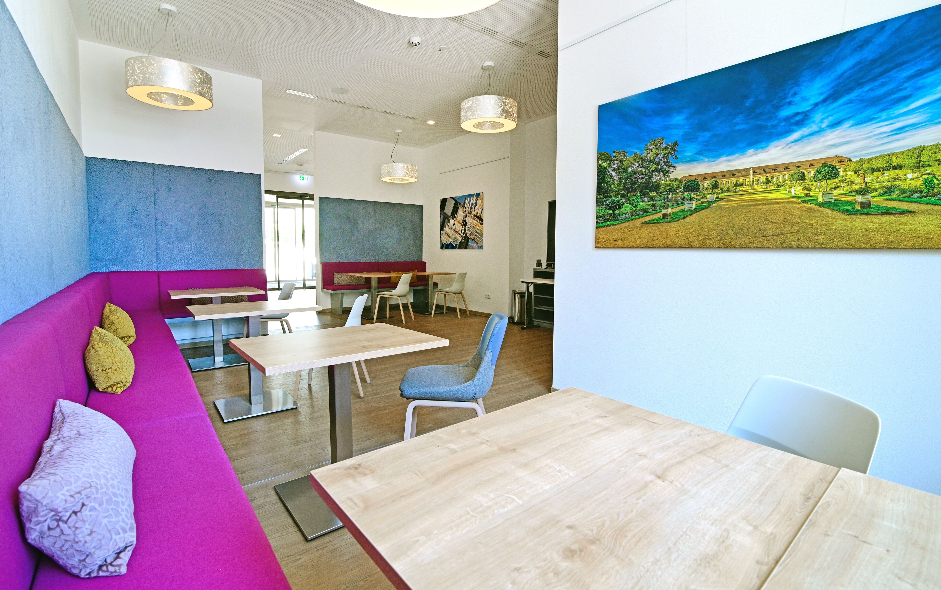 A modern interior with a wooden table, a purple sofa with cushions, and a painting of a landscape.