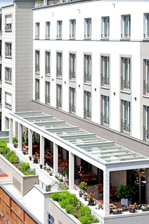 Un edificio moderno con un área de estar al aire libre cubierta, varios balcones y plantas en macetas.