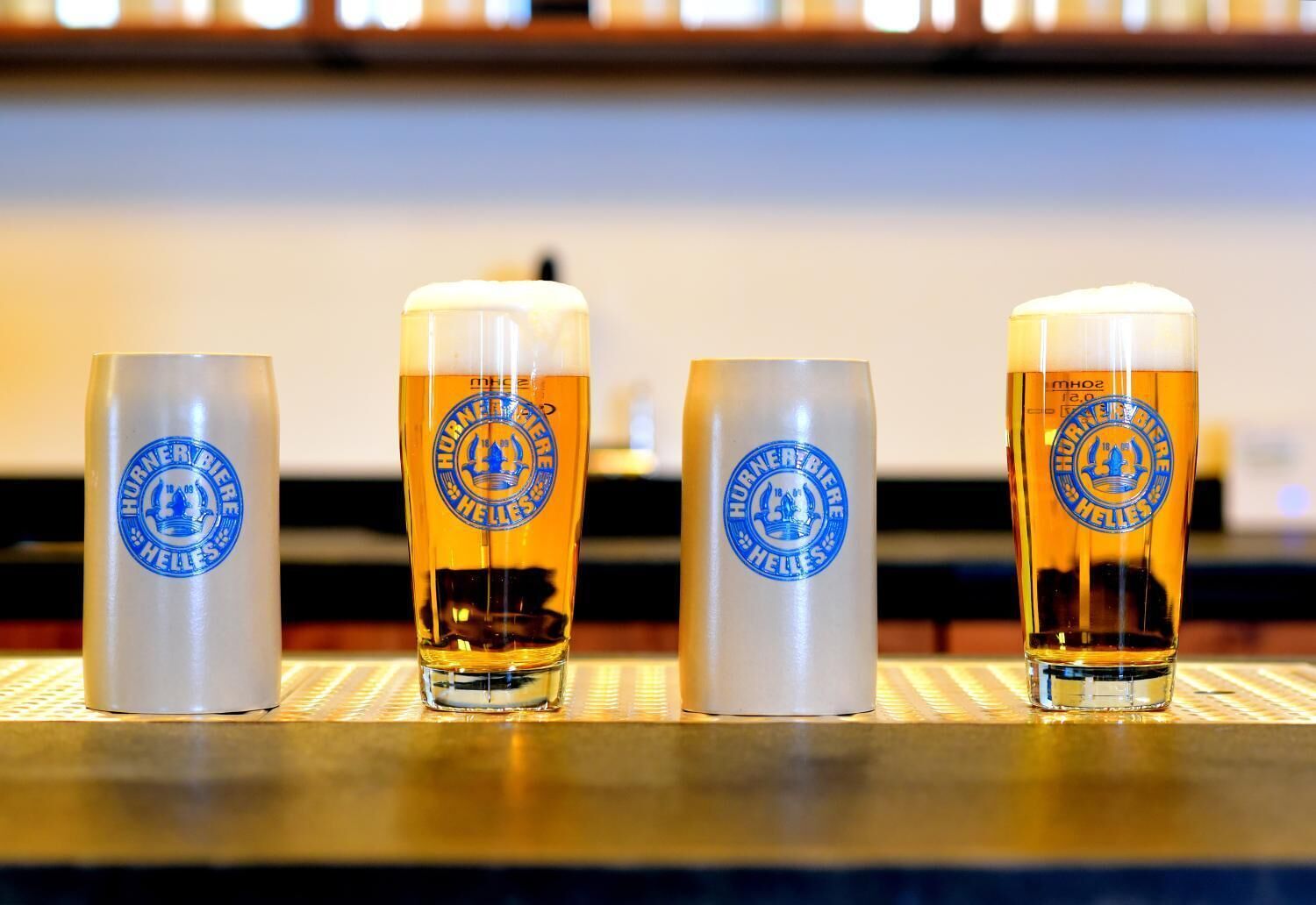 Four glasses of beer with a logo on the side, placed on a bar counter.