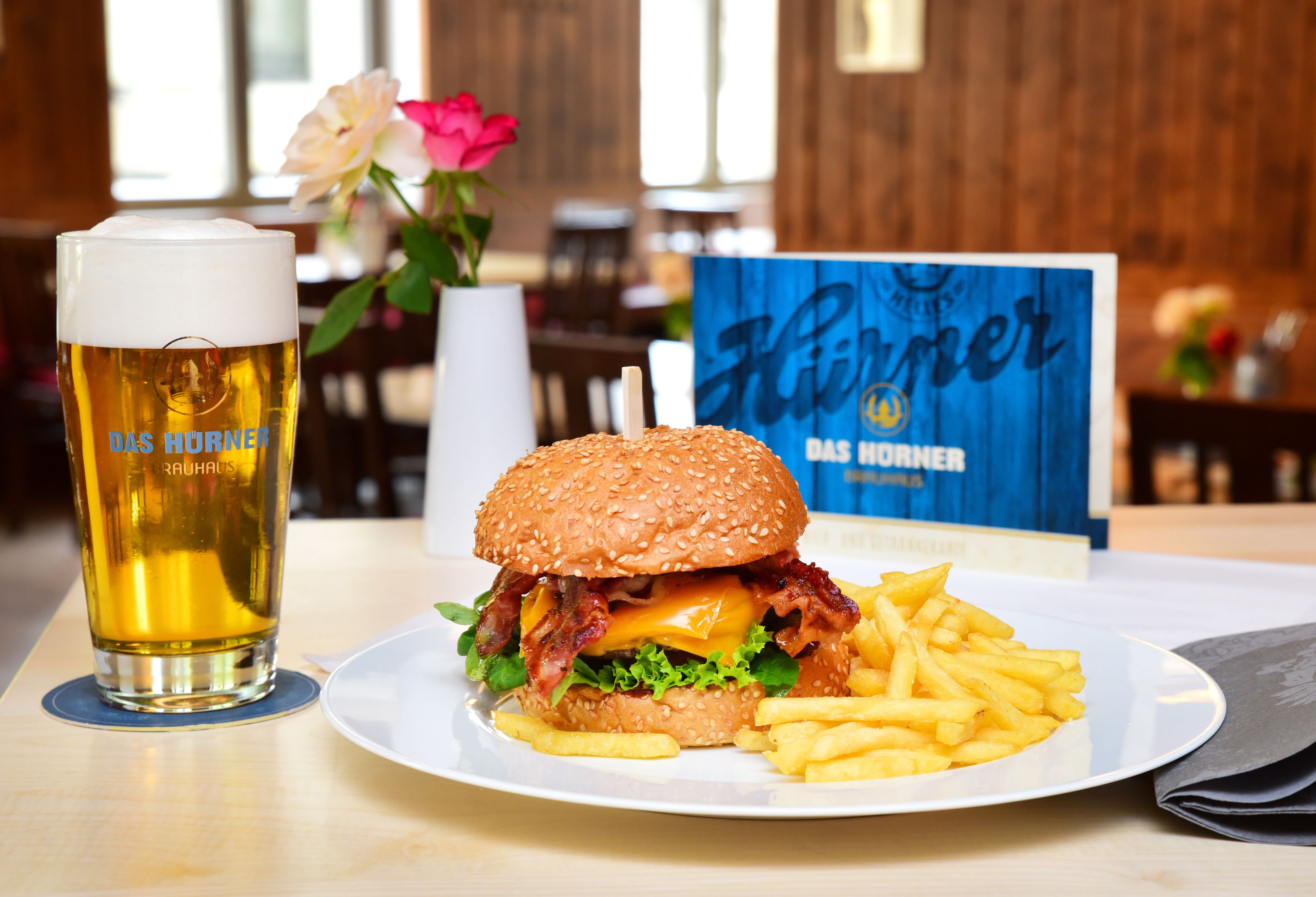 Un repas composé d’un hamburger et de frites servis dans une assiette, un verre de bière et un menu visible en arrière-plan.
