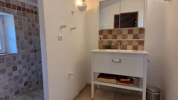 A bathroom with a tiled shower area, a sink with a mirror, and a trash bin.