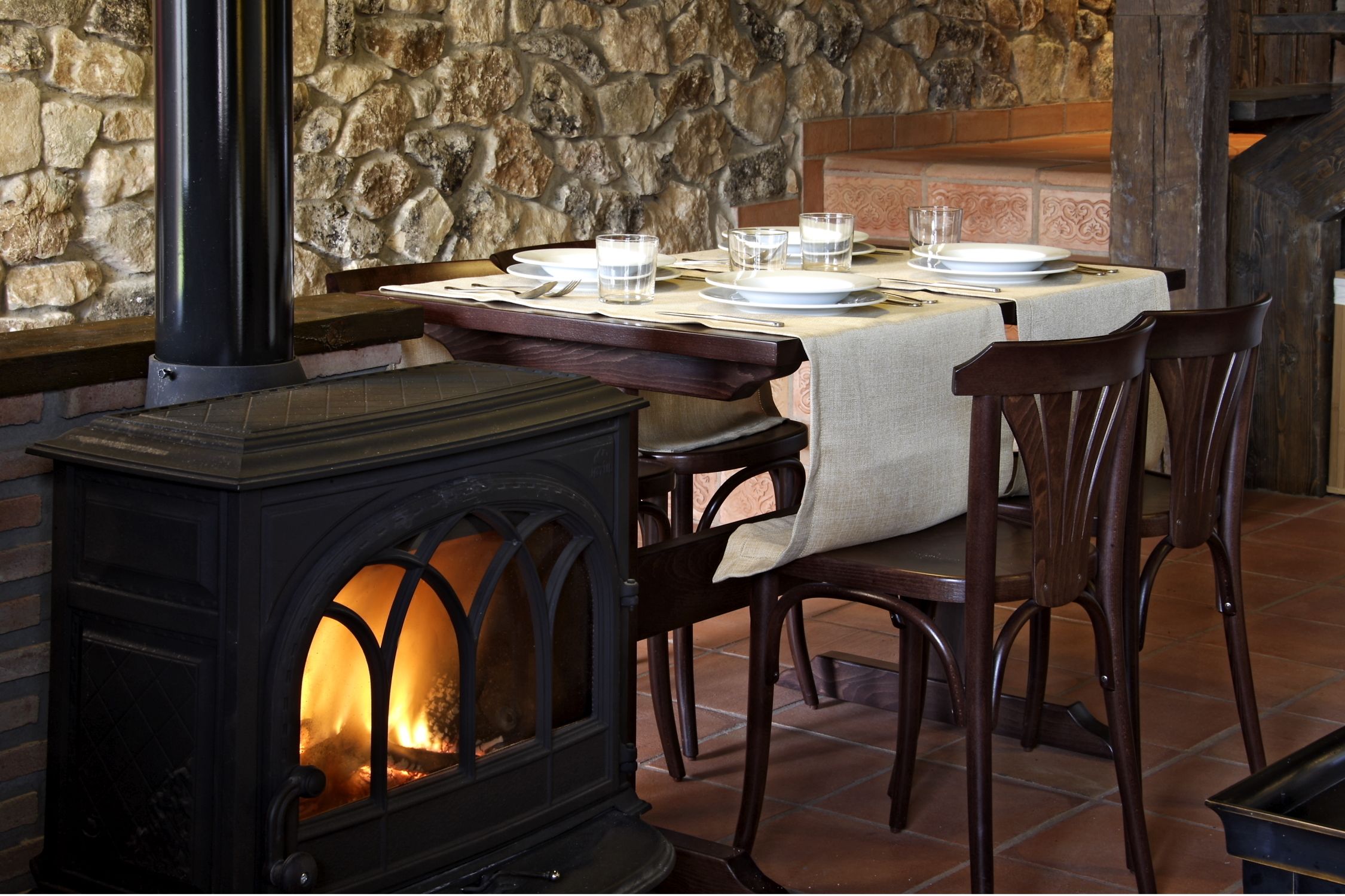 A stone wall, a fireplace with a table set for dining, and wooden chairs.