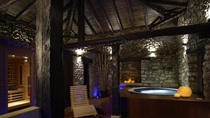 Zona de spa con paredes de piedra, bancos de madera y una bañera de hidromasaje.