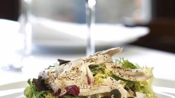 En tallrik med en blandad sallad, bestående av olika sorters grönsaker och tillbehör, tillsammans med två glas rött vin på ett bord.