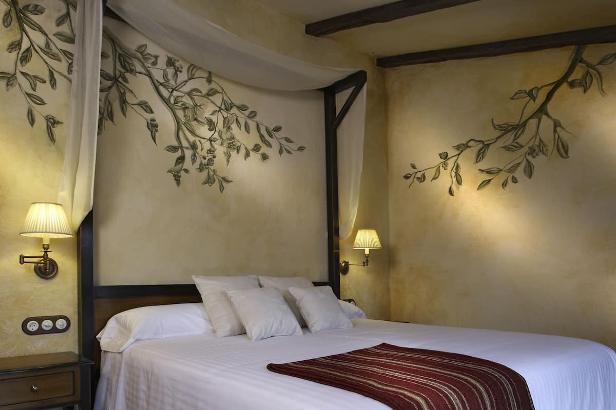 A hotel room with a large bed, two bedside lamps, a nightstand, and a wall mural of a tree branch.