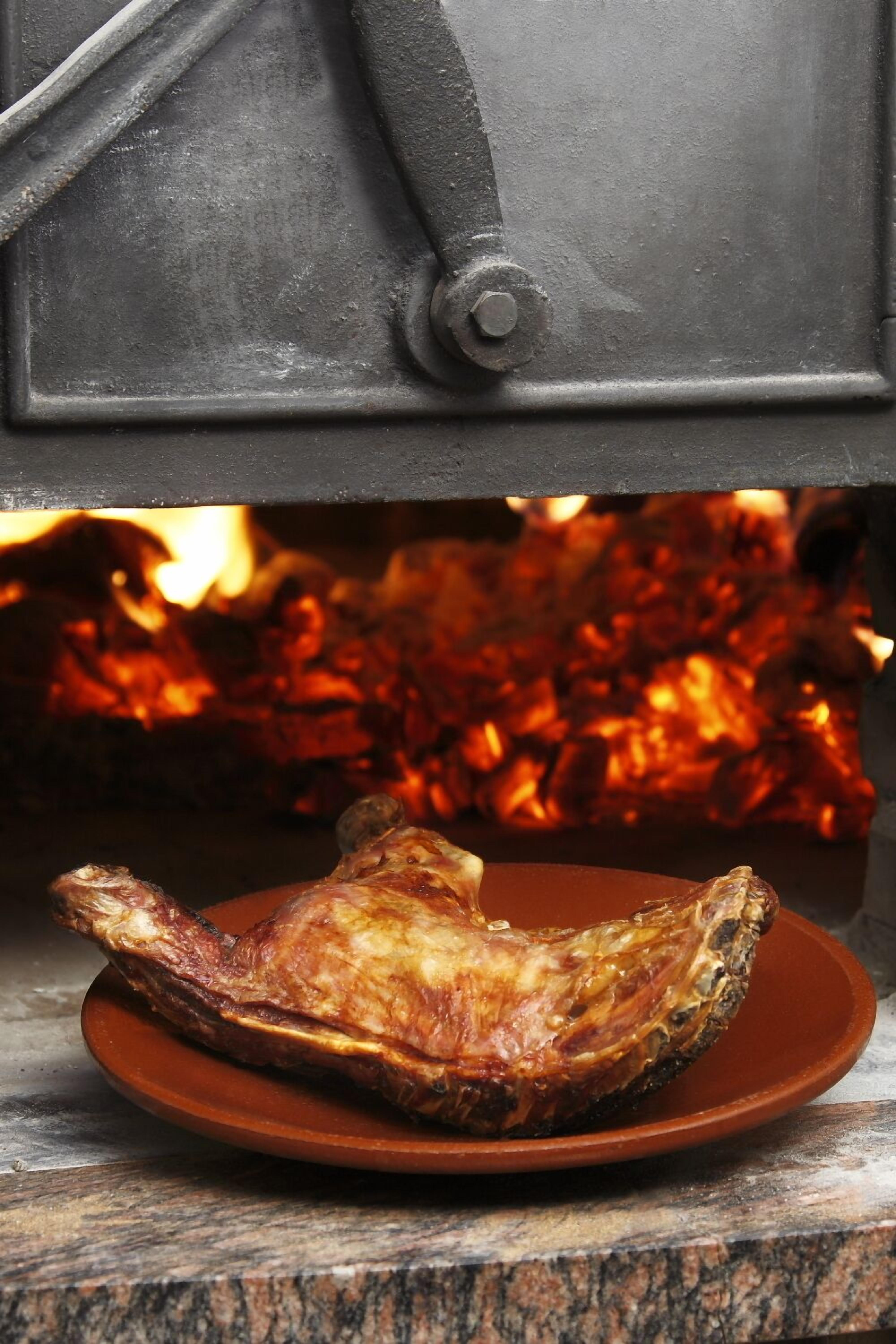 A roasted duck on a plate in front of a wood-fired oven.